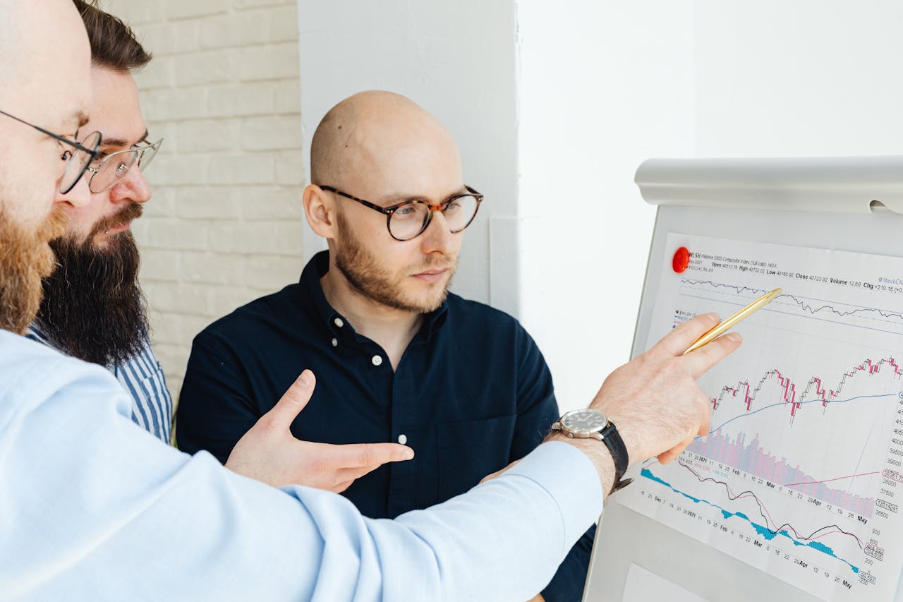 why-choose-us Three men discussing financial charts on a whiteboard during a business meeting.
